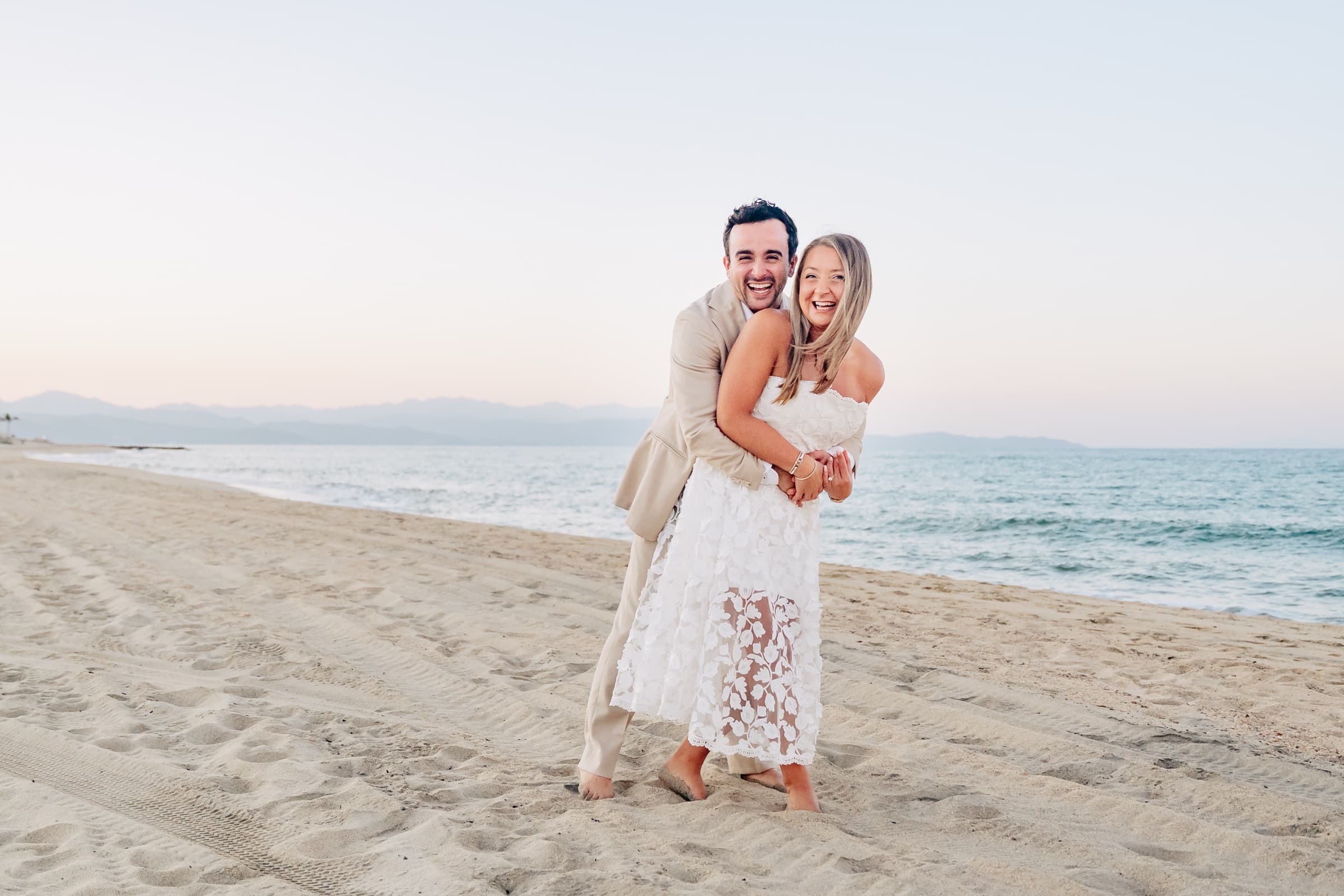 Jeffrey hugging Taylor from behind on the beach at dusk