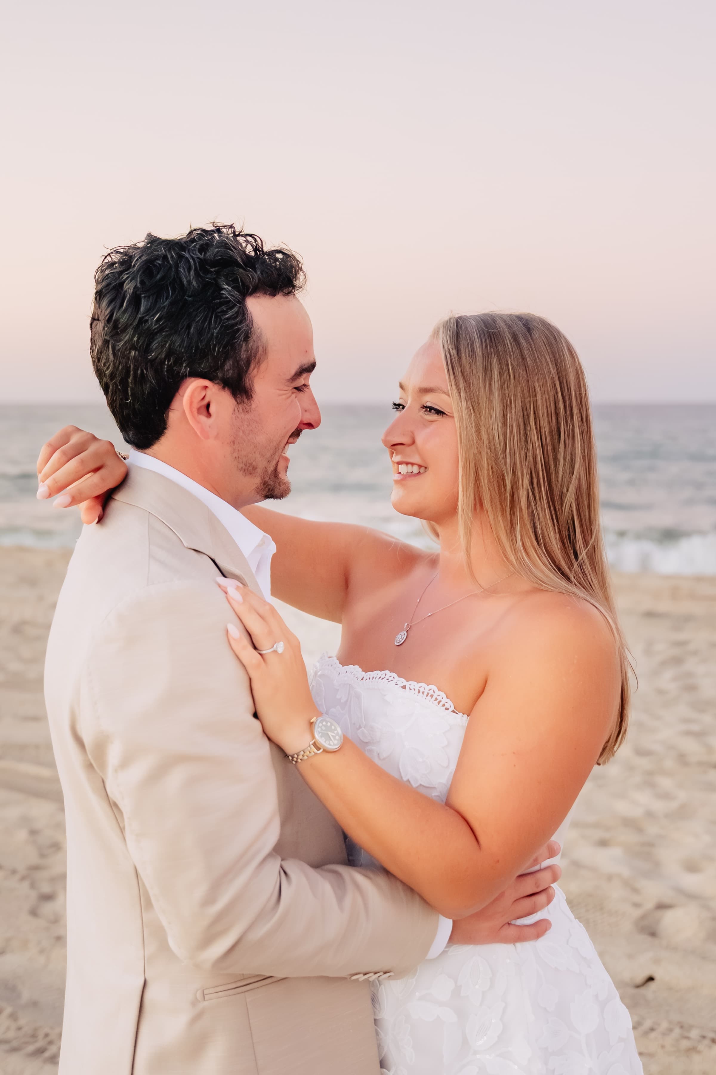 Smiling close together on the beach at sunset