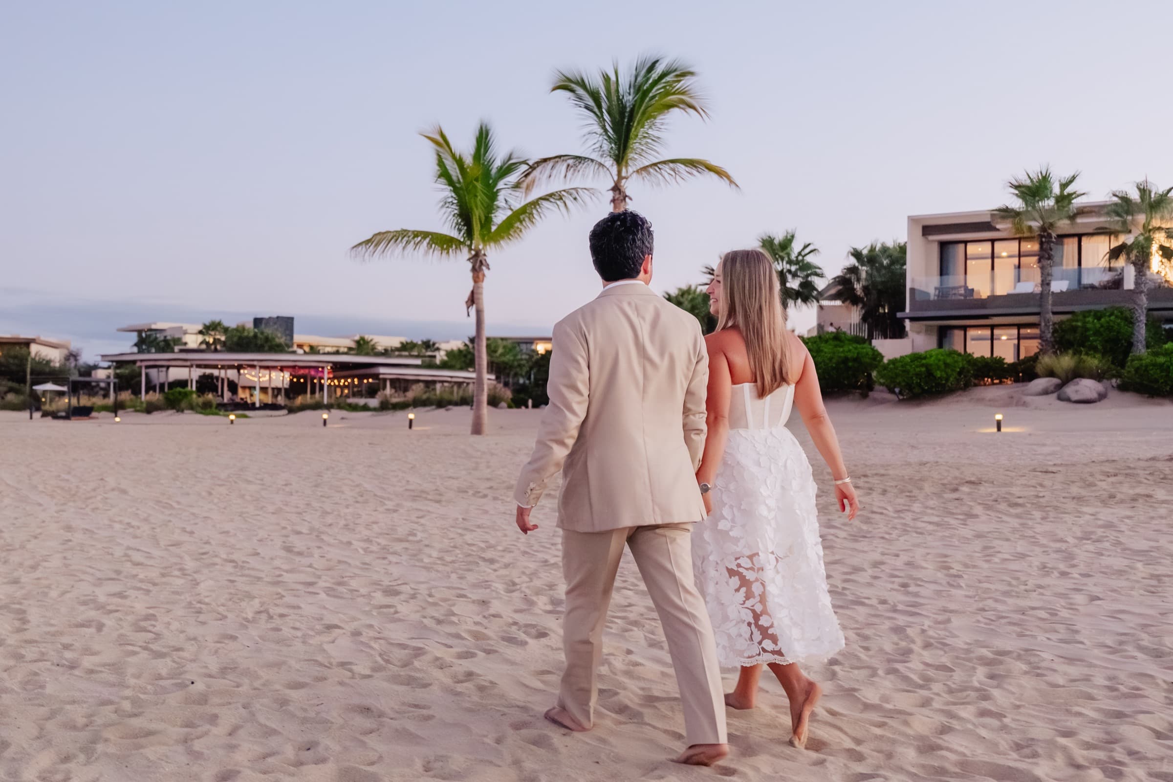 Walking away hand in hand toward a beachside resort at dusk