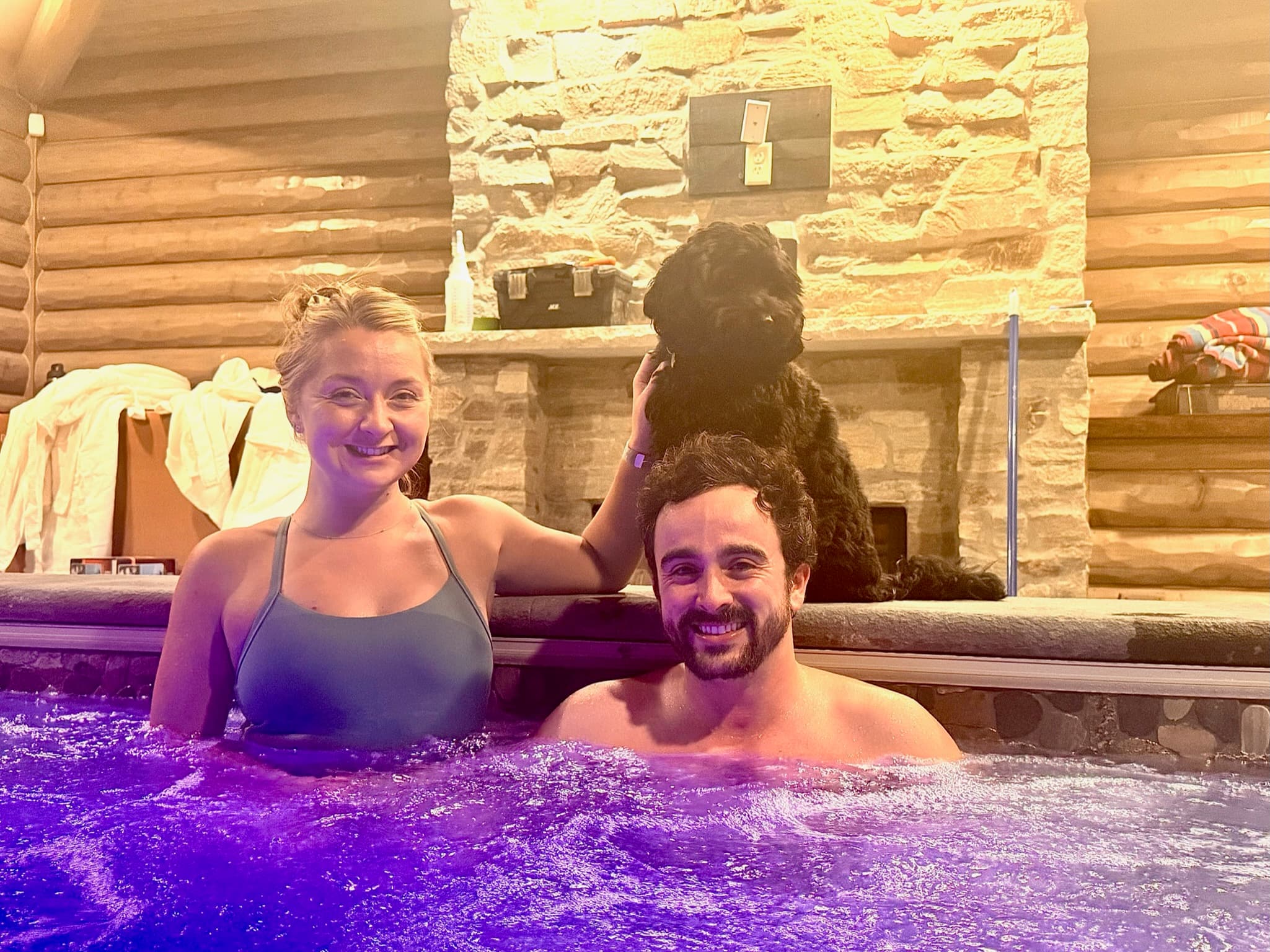 In the hot tub at a cabin with their dog perched behind