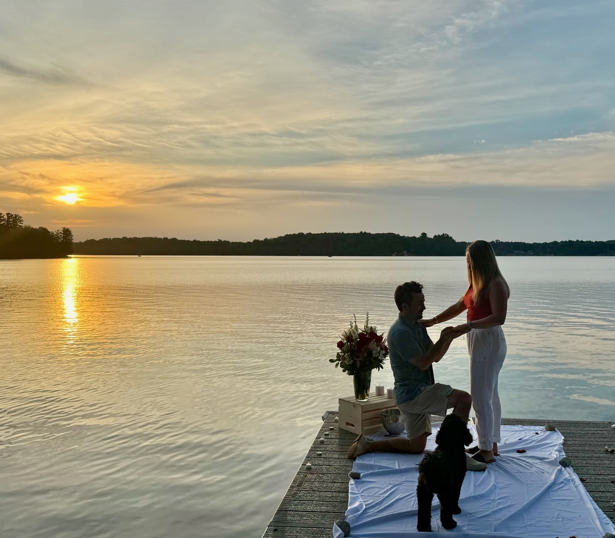 Proposal on a dock at sunset with their dog watching